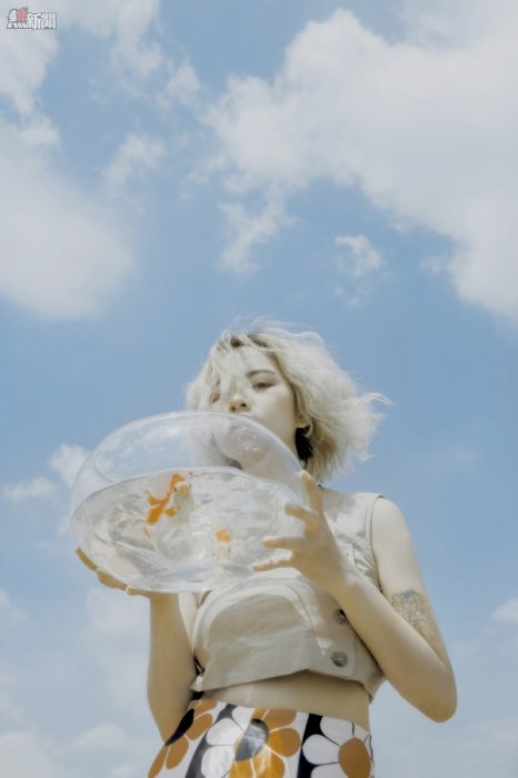 woman holding round clear glass fishbowl with live fish under white and blue sky